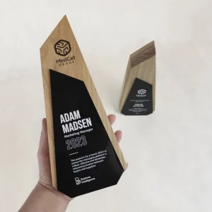 Trophée prisme en bois naturel avec plaque en acrylique noir imprimée en blanc, tenu en main